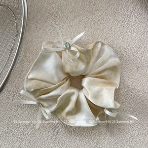 Detail of silk satin scrunchie with ink wash pattern and small white bows with crystals