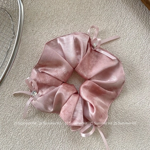 Detailed macro view of pink silk scrunchie with crystal bows and soft satin texture