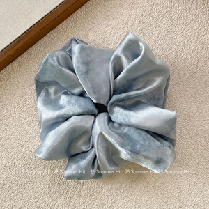 Detail of light blue satin scrunchie with wrinkled texture on beige background