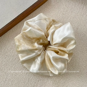Close-up of silk satin scrunchie with beige and coffee tie-dye texture and soft sheen