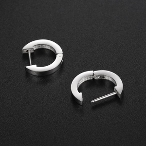 Close-up of polished silver titanium steel huggie earrings showing closure detail on black surface