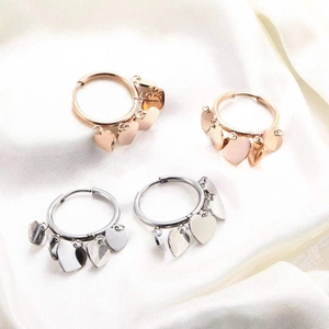 Close-up of titanium steel hoop earrings with dangling heart charms in rose gold and silver