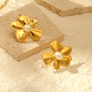 Detail of 18k gold floral stud earrings with pearls on a textured stone background
