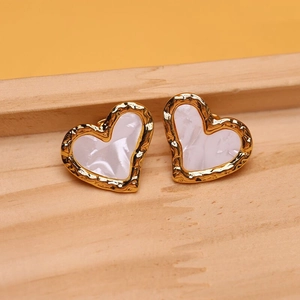 Macro shot of gold heart earrings with white inlay and hammered texture on wood tray