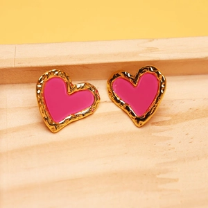 Close-up of golden heart earrings with pink enamel inlay and hammered texture on wood