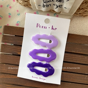 Set of three wave-shaped purple acrylic hair clips on a decorative wooden background