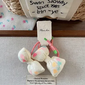 Detail of two bow hair ties with colorful dot prints on cream fabric and pink elastic ropes