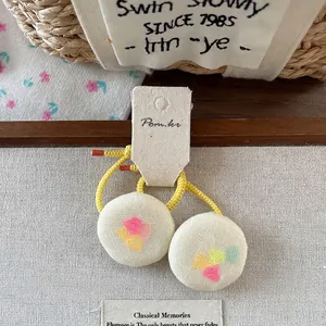 Handmade elastic hair ties with colorful printed round buttons in a rustic wood tray