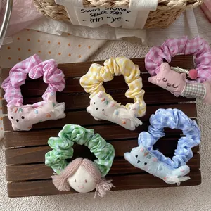 Five Korean style plaid hair scrunchies with cute cartoon charms on rustic wood background