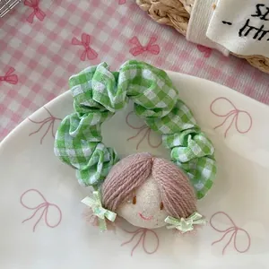 Détail d'un chouchou à carreaux verts avec une tête de poupée faite à la main en tissu