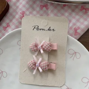 Détail de barrettes cœur à carreaux roses avec nœud et perles sur carton