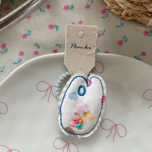Détail d'un chouchou en tissu blanc avec broderie bleue, accents d'étoiles et perles