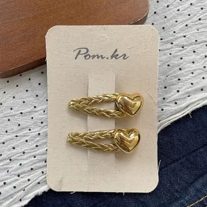 Close-up of two gold heart hair clips with woven metal texture on a display card
