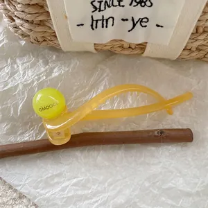 Detail of yellow translucent hair clip with neon green decorative ball on wood branch