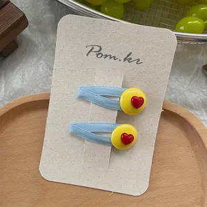Detail of blue fabric hair clip with yellow round accent and red heart on paper card