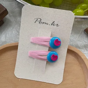 Detail of pink fabric-wrapped hair clips with colorful resin button charms on display card