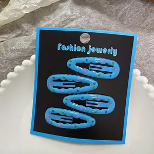 Close-up of four blue wavy snap hair clips with colorful polka dots on display card