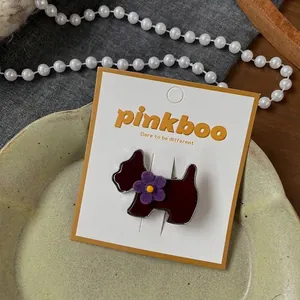Detailansicht einer dunkelroten Haarspange in Hundeform mit violetter Blume auf Karte