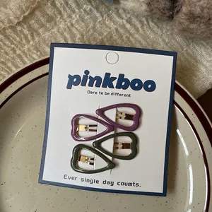 Close-up of heart-shaped metal hair clips in purple and dark green on a card