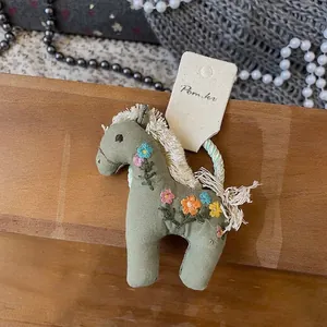 Détail d'un charm poney vert olive brodé avec des fleurs colorées et des glands blancs