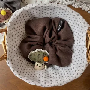Détail d'un chouchou marron avec breloque champignon en peluche dans un panier tissé