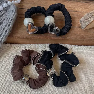 Scrunchies in raso fatti a mano con perle e ciondoli a cuore su sfondo di legno vintage
