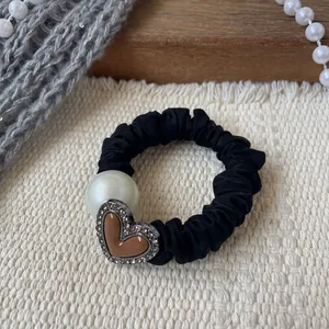 Dettaglio dell'elastico nero a pieghe con perla e ciondolo a cuore con strass