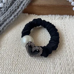 Dettaglio di elastico scrunchie nero con grande perla e ciondolo a cuore con strass brillanti