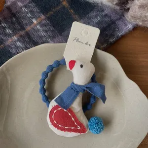 Detail eines Stoff-Haargummis mit weißem Gänseanhänger und blauem Bommel auf Keramiktablett