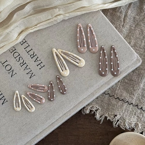 Polka dot metal BB hair clips in earthy tones displayed on a minimalist linen background