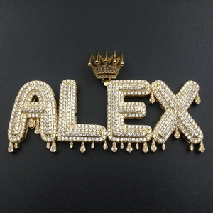 Close-up of golden ALEX letter pendant with crown and zircon stones on black background