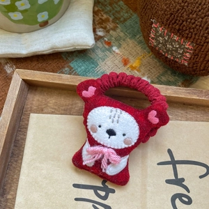 Détail d'un chouchou en feutre rouge avec broderie mignonne et nœud rose sur plateau