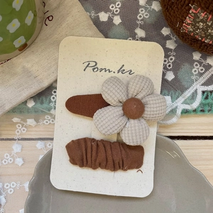 Détail d'une pince à cheveux plissée marron et d'une fleur à carreaux beige sur carte