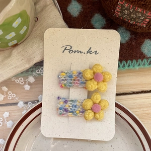 Detail von handgestrickten Blumen-Haarspangen mit gelben Blüten auf einer Karte