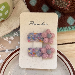 Detail von zwei handgestrickten Blumen-Haarspangen mit rosa Blüten auf Spitzenhintergrund