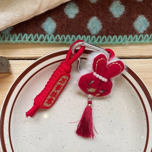 Detail of red plush bunny keychain with pearl accent, embroidery, and festive tassel