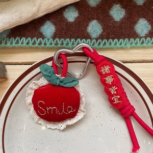Detail of red plush apple keychain with Smile embroidery and heart-shaped metal clip