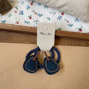 Close-up of navy blue hair ties with droplet leather charms and brown hand-stitching detail