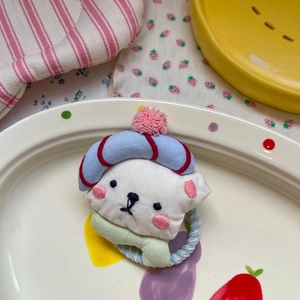 Détail d'un chouchou ours brodé avec bonnet à pompon coloré sur une assiette en céramique