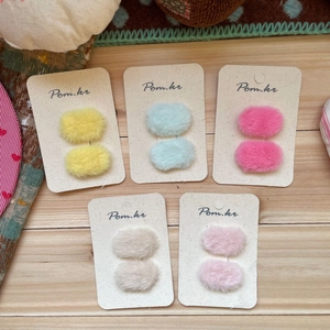 Five pairs of colorful plush oval hair clips on cards over a light wood background