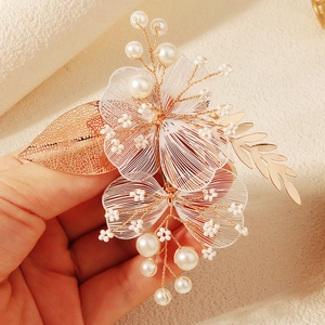 Détail d'une pince à cheveux de mariée avec feuilles dorées, pétales et perles