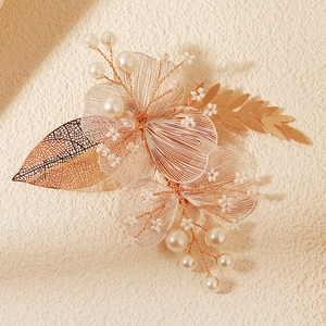 Détail d'une pince à cheveux de mariée avec pétales en fil doré, perles et feuille en métal