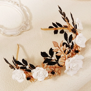 Detailed close-up of retro gold headband with black leaves and white rose decorations