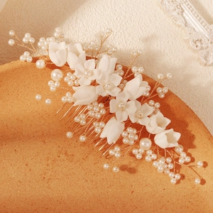 Close-up of handmade white resin flowers and ivory pearls on a golden metal bridal hair comb
