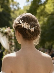 Détail d'un peigne de mariée avec feuilles dorées, fleurs de soie et perles sur un chignon de mariage