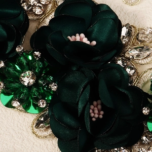 Detailed macro view of dark green satin fabric flower with emerald rhinestone embellishment