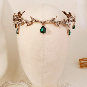 Detail of vintage leaf crown with drop-shaped green gems and golden alloy texture