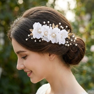 Close-up of bridal hair comb with white fabric flowers and golden leaves on model