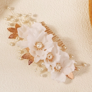 Detailed close-up of handmade white fabric flowers and pearls on a gold bridal hair comb