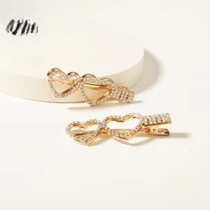 Détail de deux barrettes dorées en strass avec motifs de cœurs sur un support blanc